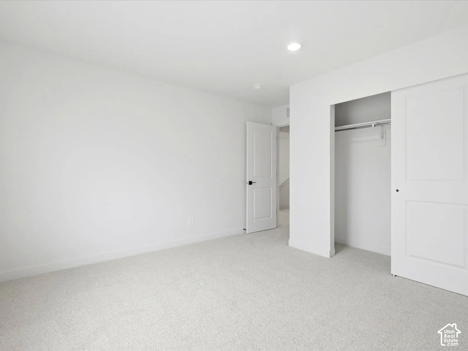 Neutral-toned wall-to-wall carpeting, recessed ceiling lighting, a closet with a sliding panel door, and a multi-panel interior door with matte black hardware