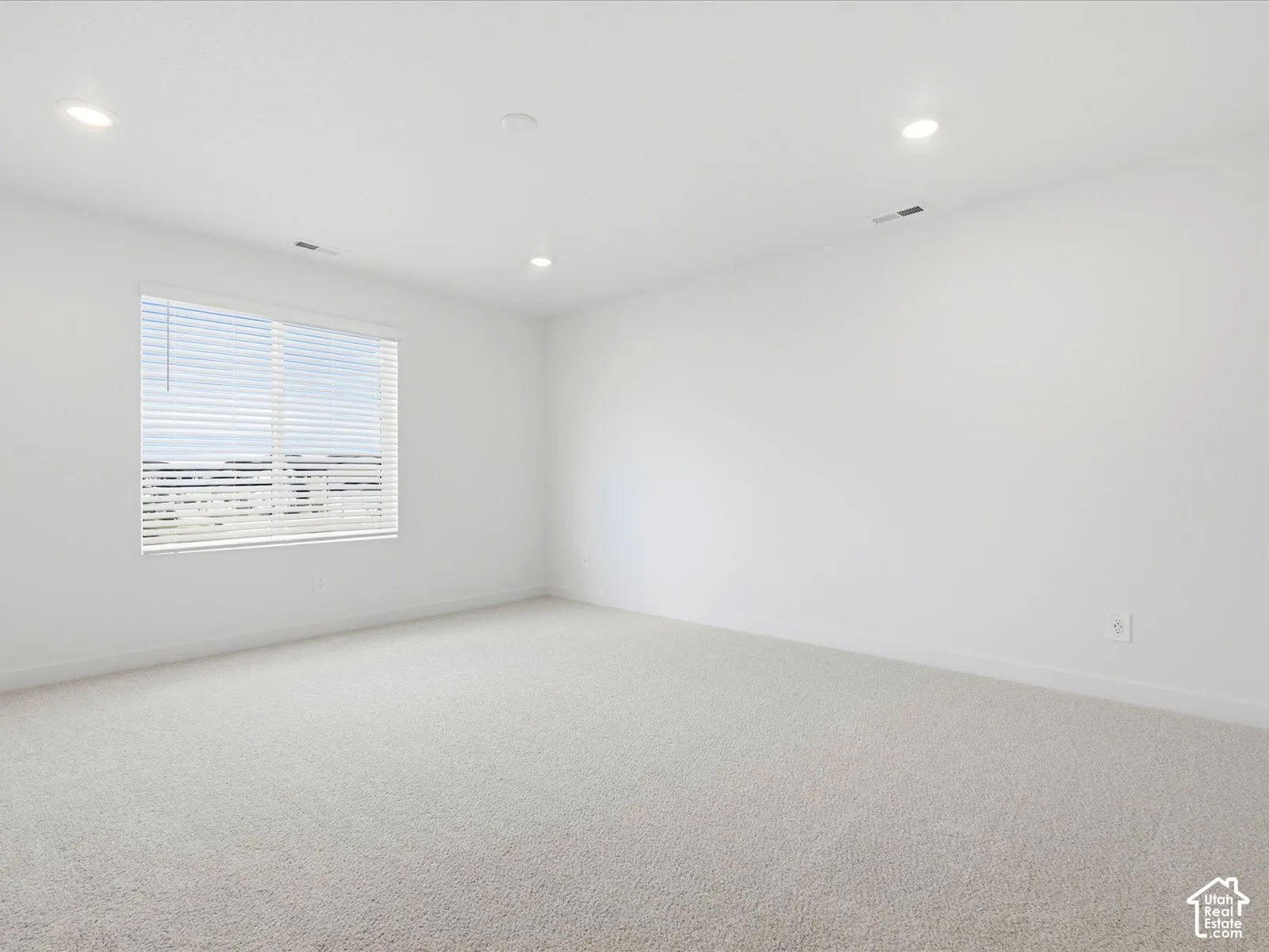 Neutral-toned carpeting, recessed ceiling lighting, and a window fitted with horizontal blinds