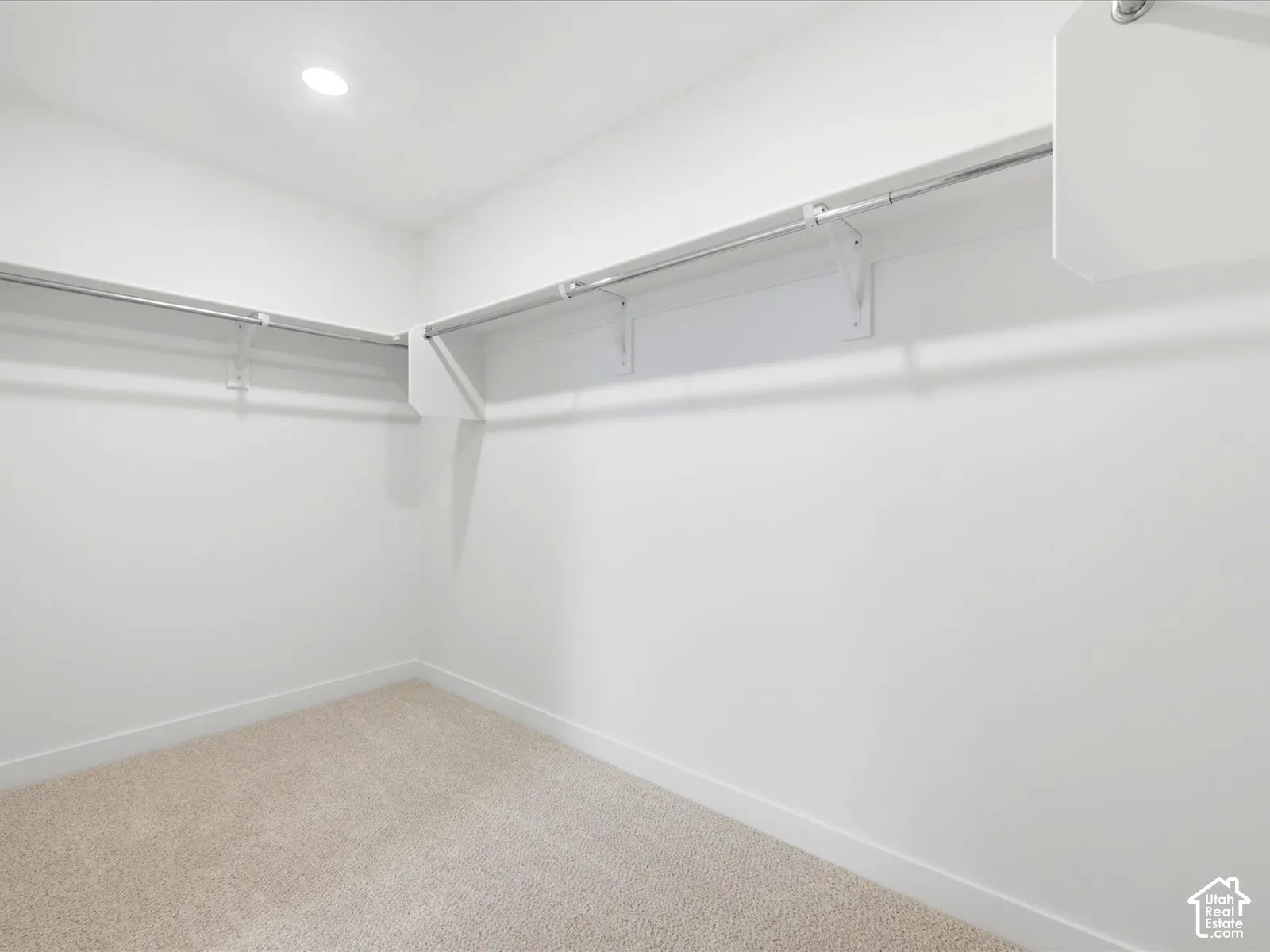 Walk-in closet featuring neutral carpeting, recessed lighting, and wall-mounted white shelving with metal hanging rods