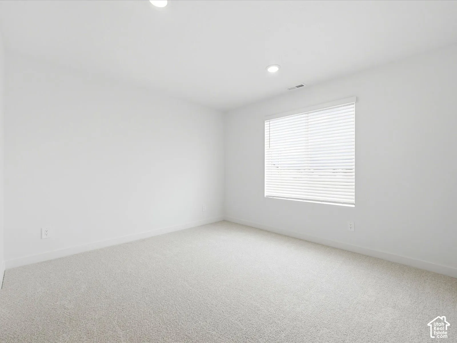 Neutral-toned carpeting, recessed ceiling lighting, and a window fitted with horizontal blinds