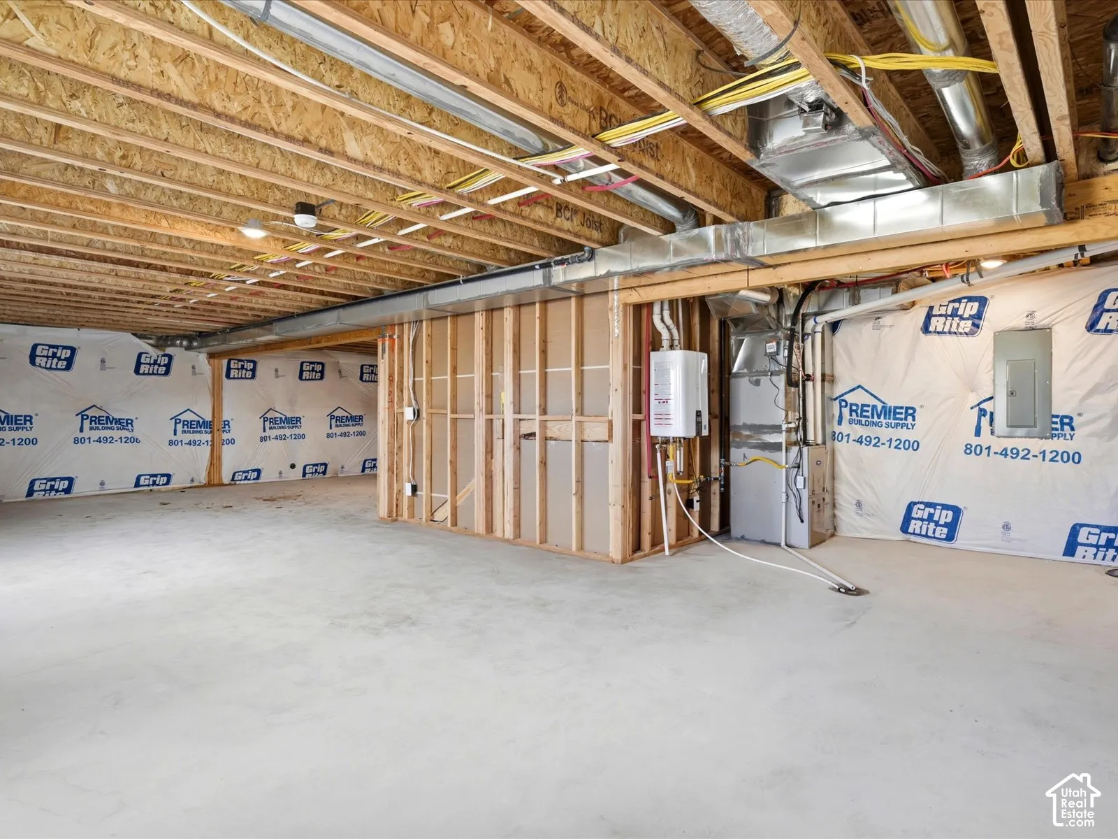 Unfinished basement featuring exposed wood joists, poured concrete flooring, wall-mounted tankless water heater, and mechanical furnace unit