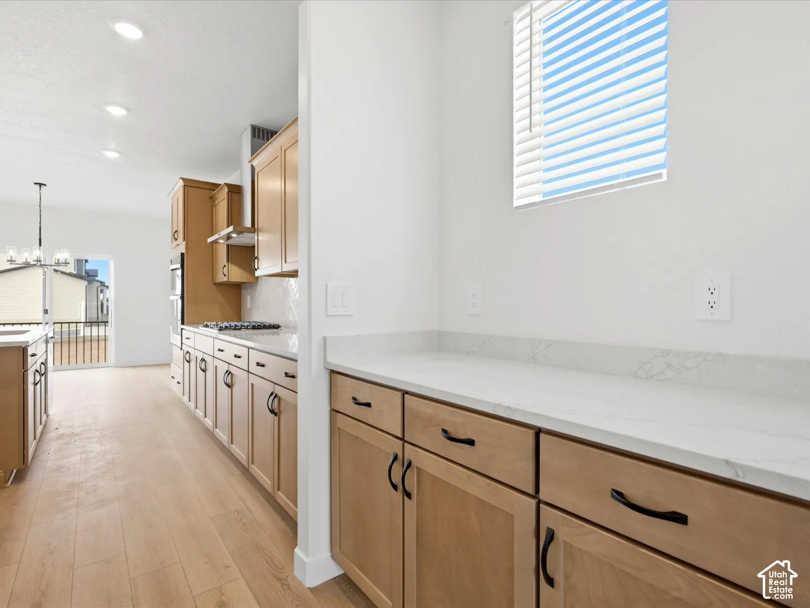 **DISCLAIMER**  Interior package may vary. Kitchen featuring light wood-finish cabinetry, white stone-composite countertops, recessed lighting, and wood-finish flooring