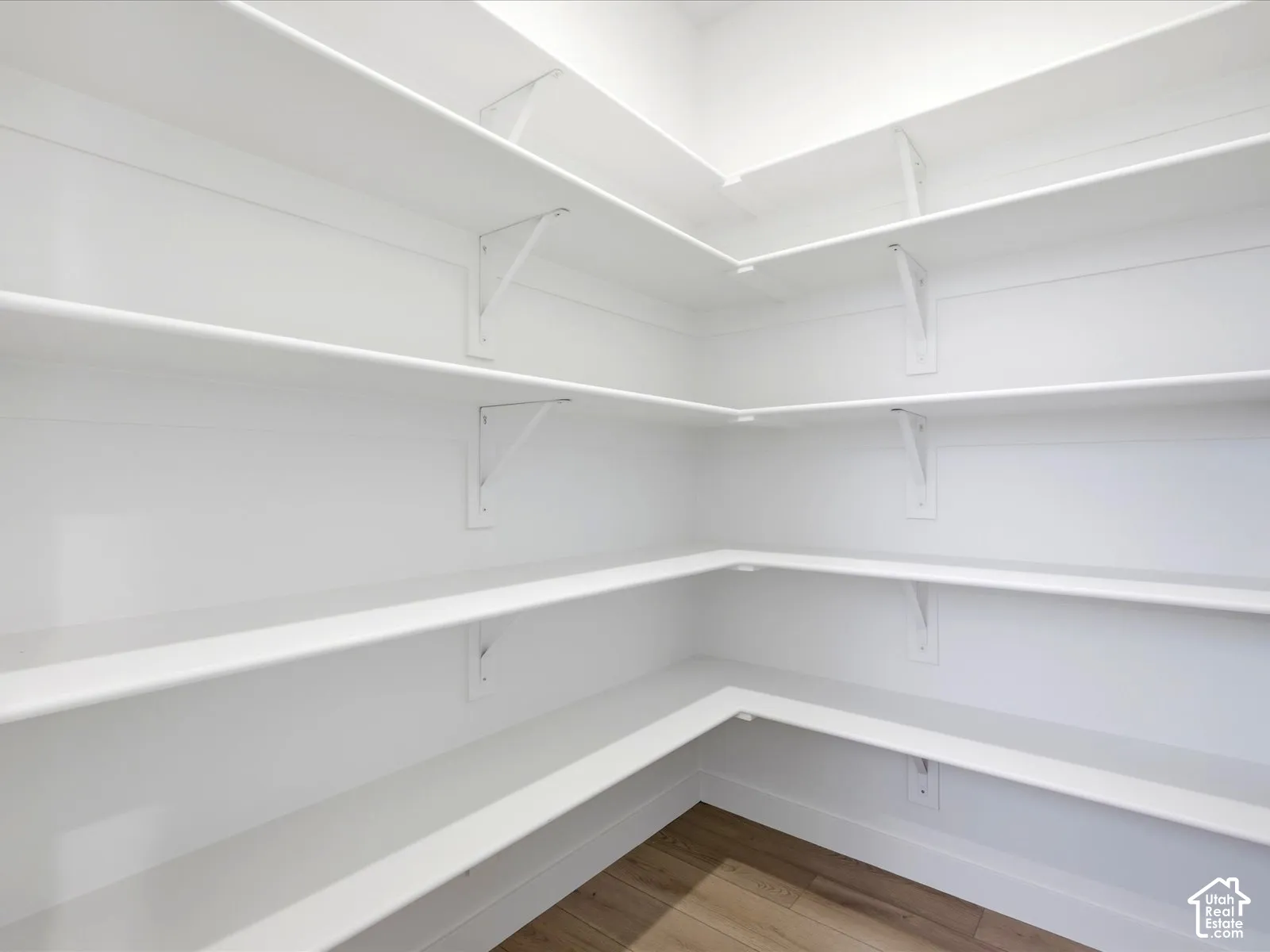 Walk-in storage space featuring multi-level wrap-around shelving supported by metal brackets and wood-finish flooring