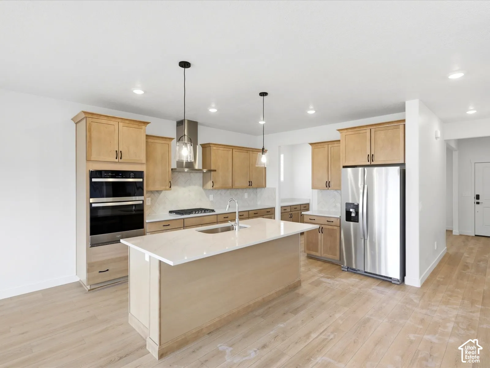 **DISCLAIMER**  Interior package may vary. Kitchen featuring light-finish cabinetry, a central island with a quartz countertop, stainless steel appliances, a wall-mounted range hood, and wood-finish flooring