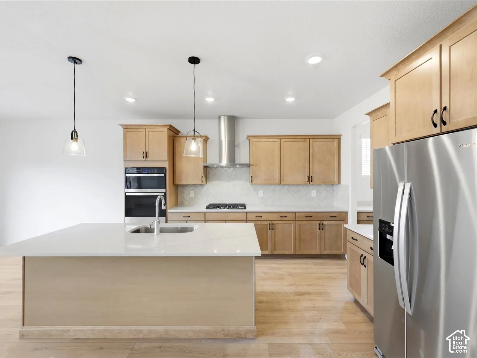**DISCLAIMER**  Interior package may vary. Kitchen featuring a central island with a solid surface countertop, light wood-finish cabinetry, stainless steel appliances, a built-in wall oven, and wood-finish flooring