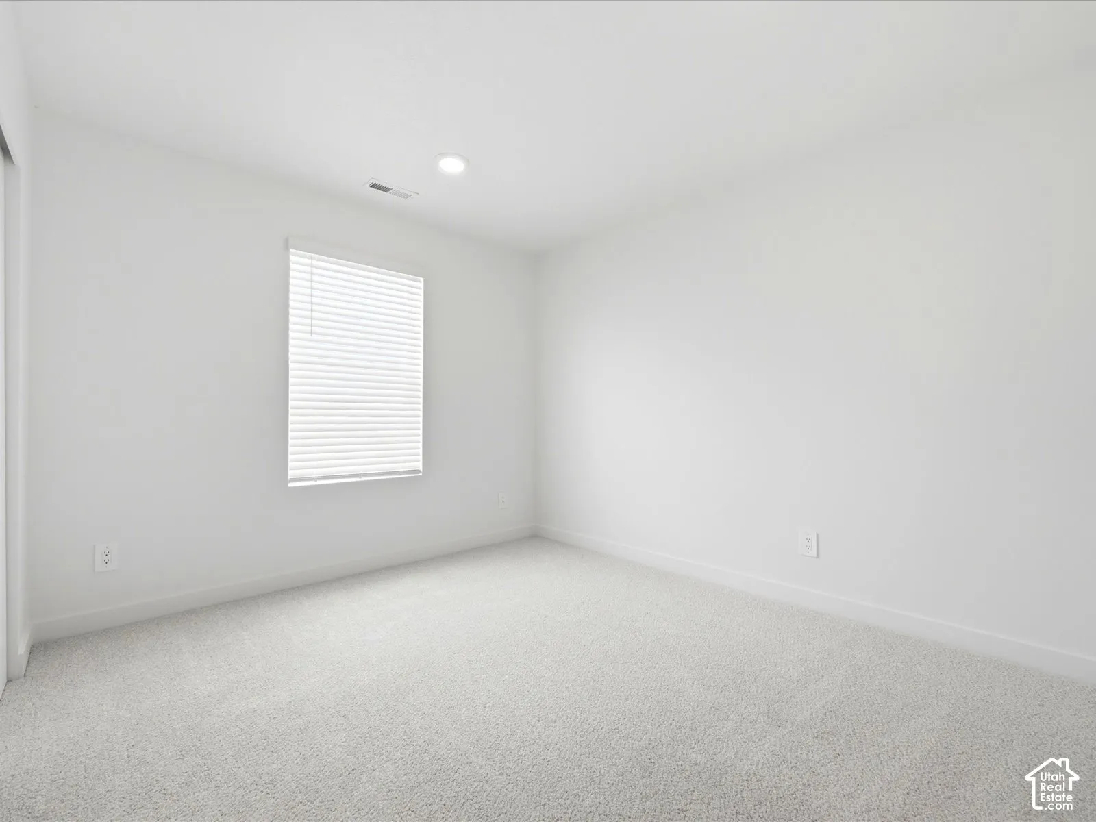 Neutral-toned carpeting, recessed ceiling lighting, and a window with horizontal blinds