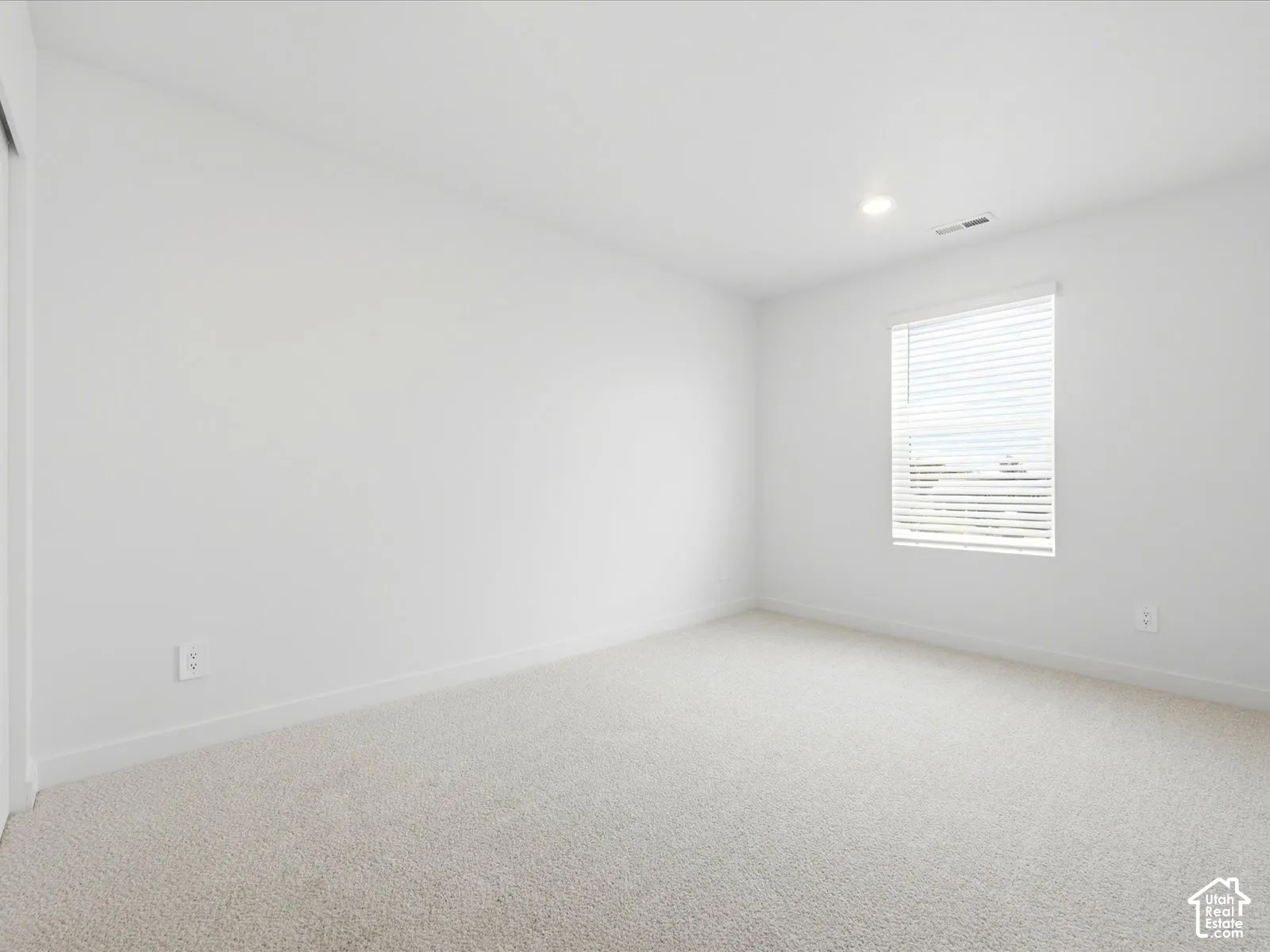 Neutral-toned carpeting, recessed ceiling lighting, and a window featuring horizontal blinds