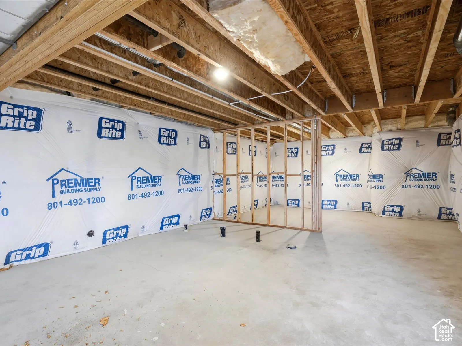 Unfinished lower level featuring exposed wood joists, vapor barrier wall wrap, concrete flooring, and wood-frame wall partitions