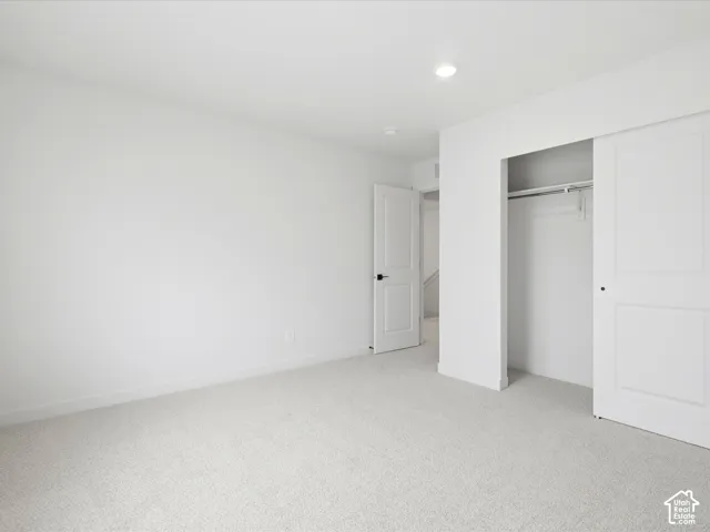Neutral-toned wall-to-wall carpeting, recessed ceiling lighting, a closet with a sliding panel door, and a multi-panel interior door with matte black hardware