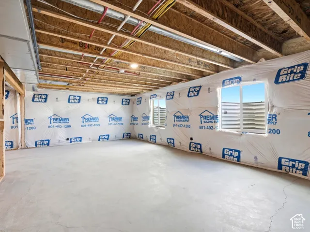 Unfinished basement area featuring a concrete floor, exposed wood-joist ceiling, and two egress windows with corrugated metal window wells
