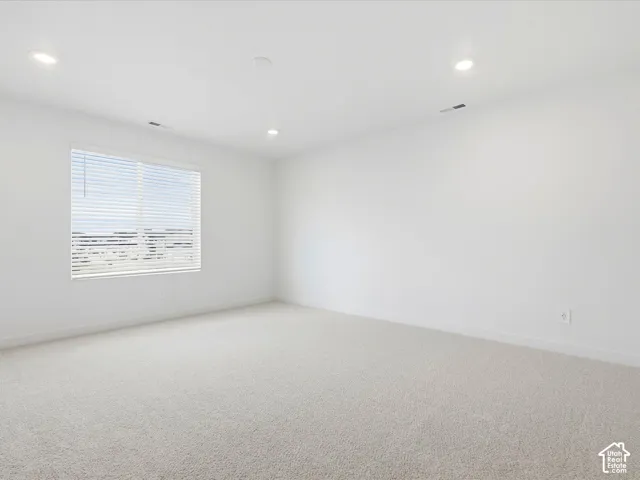 Neutral-toned carpeting, recessed ceiling lighting, and a window fitted with horizontal blinds