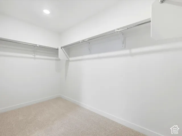 Walk-in closet featuring neutral carpeting, recessed lighting, and wall-mounted white shelving with metal hanging rods