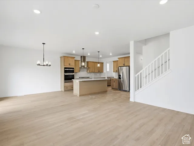 **DISCLAIMER**  Interior package may vary. Open-concept living space featuring wood-finish flooring, recessed lighting, a central kitchen island, stainless steel appliances, and a staircase with a white balustrade