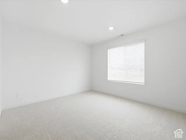 Neutral-toned carpeting, recessed ceiling lighting, and a window fitted with horizontal blinds