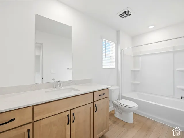 **DISCLAIMER**  Interior package may vary. Bathroom featuring a wood-finish vanity with a stone-composite countertop, undermount sink, frameless wall-mounted mirror, and wood-finish flooring