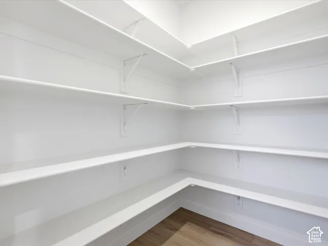 Walk-in storage space featuring multi-level wrap-around shelving supported by metal brackets and wood-finish flooring