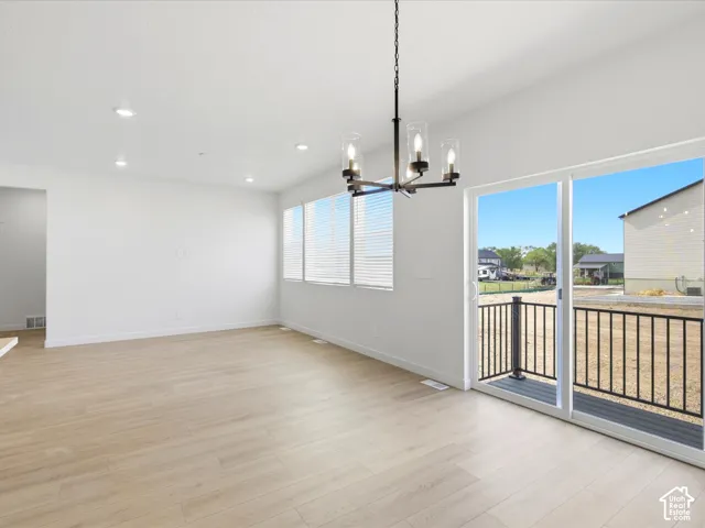 **DISCLAIMER**  Interior package may vary. Open-concept interior featuring wood-finish flooring, recessed lighting, a modern multi-light chandelier, and sliding glass doors with access to an exterior deck with a metal railing