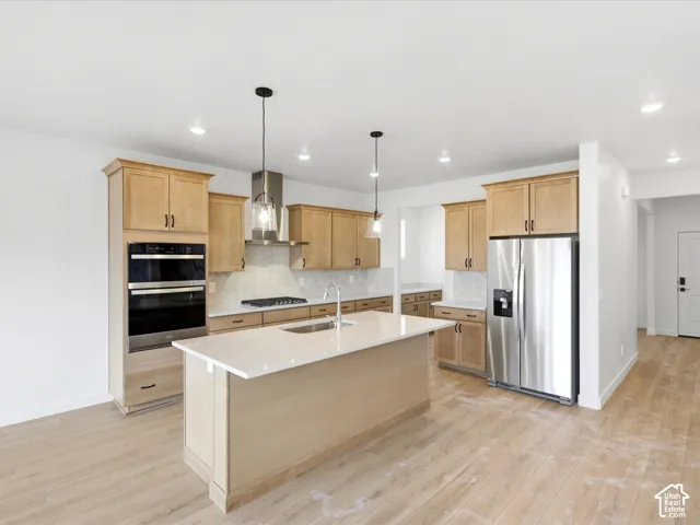 **DISCLAIMER**  Interior package may vary. Kitchen featuring light-finish cabinetry, a central island with a quartz countertop, stainless steel appliances, a wall-mounted range hood, and wood-finish flooring