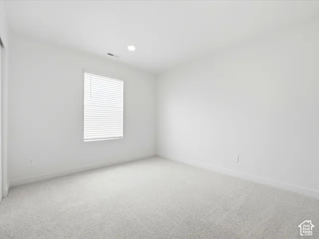Neutral-toned carpeting, recessed ceiling lighting, and a window with horizontal blinds