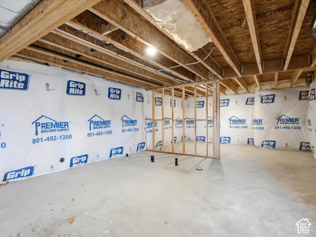Unfinished lower level featuring exposed wood joists, vapor barrier wall wrap, concrete flooring, and wood-frame wall partitions