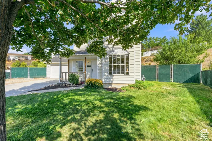 Two-story home with light-colored siding, a covered front porch, concrete driveway, attached garage, and chain-link perimeter fencing