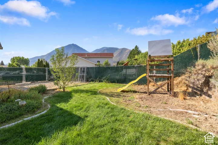 Backyard featuring a grass lawn, metal chain-link perimeter fencing, and prominent mountain scenery