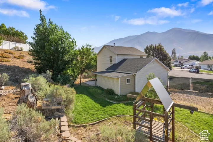 Exterior featuring siding, asphalt shingle roof, terraced landscaping with stone retaining wall, and mountain backdrop