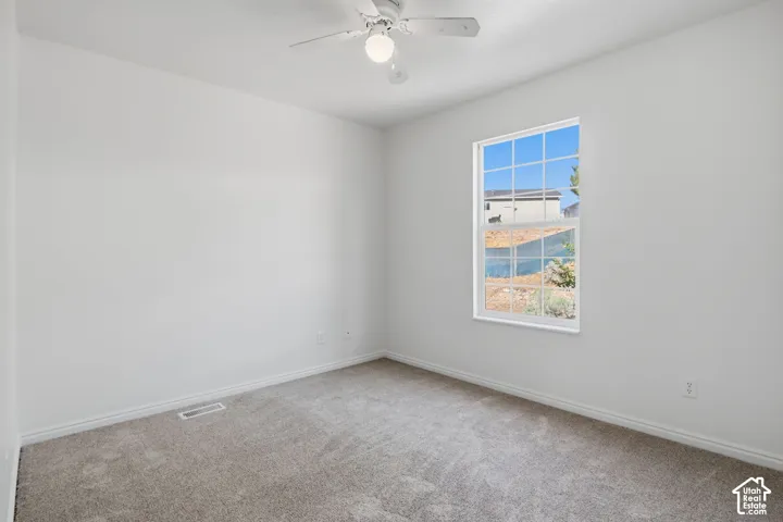 Neutral-toned wall-to-wall carpeting, single-hung window with decorative grilles, and ceiling fan with integrated light fixture