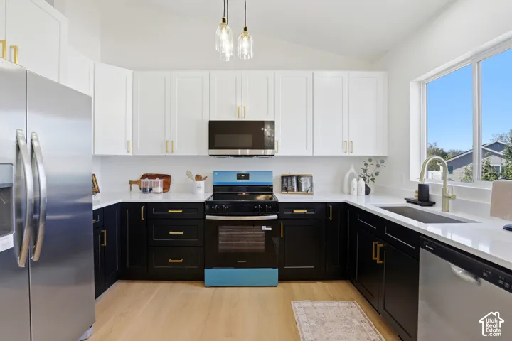 Kitchen featuring two-tone cabinetry, quartz countertops, stainless steel appliances, brushed gold hardware, and wood-finish flooring