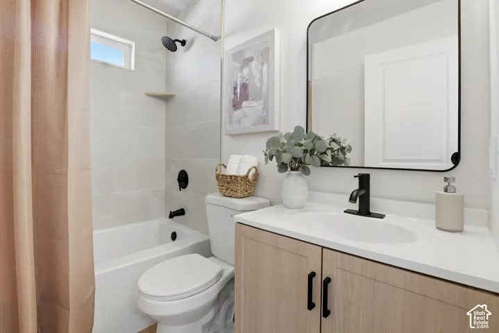 Bathroom featuring a light wood-finish vanity with a white countertop, rectangular mirror with a black frame, matte black fixtures, and a shower-tub combination with large-format wall tile