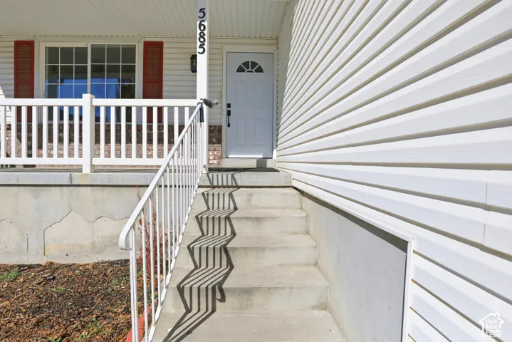 Exterior entry featuring white horizontal siding, a covered porch with white railing, and a front door with a half-moon light