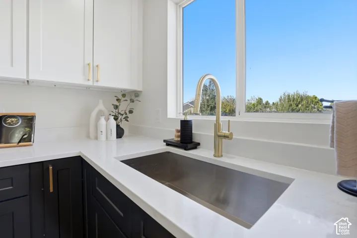 Kitchen featuring white upper cabinetry, dark lower cabinetry, quartz countertops, an undermount stainless steel farmhouse sink, and a brass gooseneck faucet