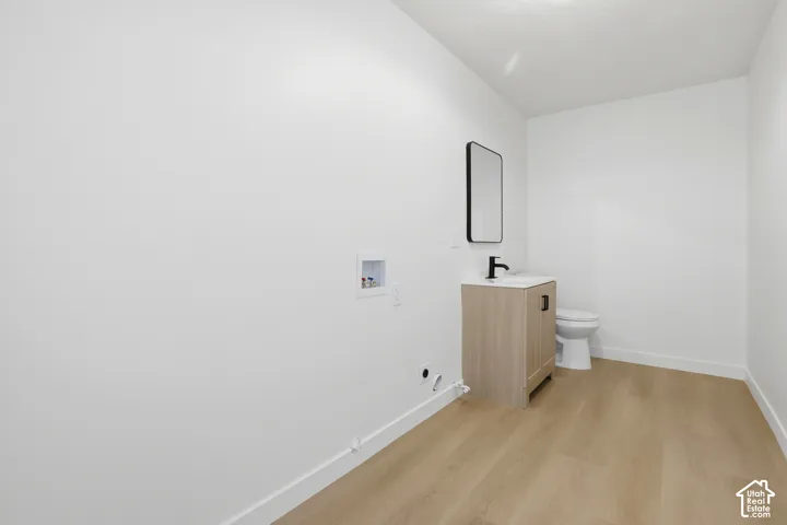 Wood-finish flooring, vanity with a white top and black hardware, rectangular wall-mounted mirror, matte black faucet, and white porcelain toilet