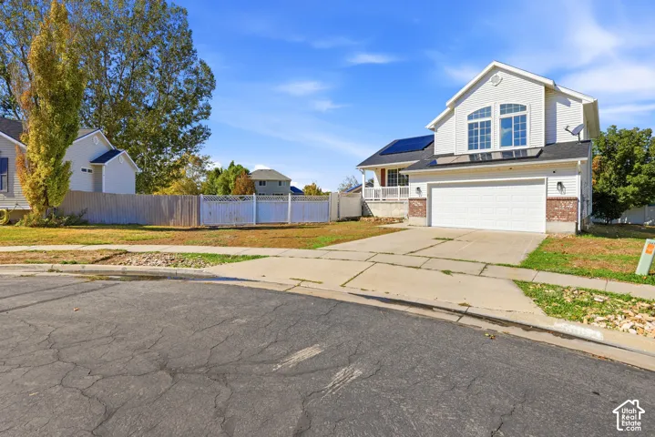 Two-story residence featuring light-colored horizontal siding, brick accents, solar panels, an attached two-car garage, and white vinyl privacy fencing