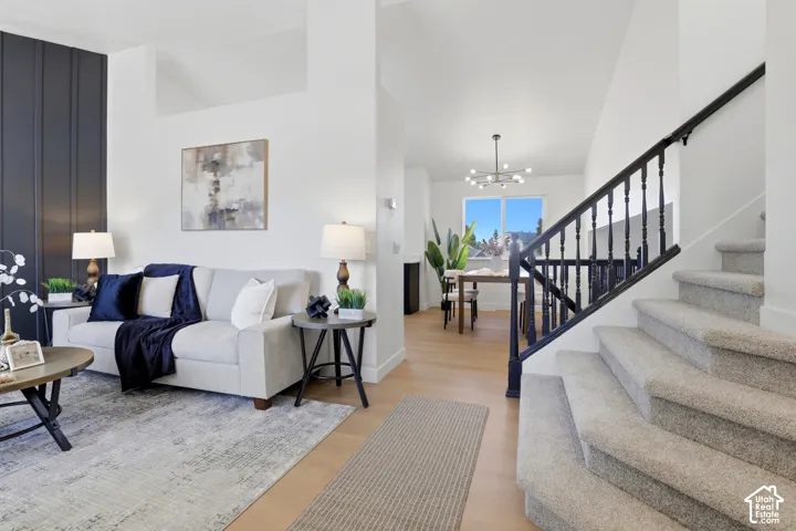 Vaulted ceilings, vertical accent wall, light-toned wood-finish flooring, staircase with a dark-finished railing, and a multi-arm modern light fixture