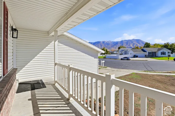 Covered front porch featuring white vinyl siding, a painted wood-style railing, an exterior wall-mounted lantern, and mountain backdrop