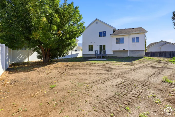 Backyard featuring horizontal siding, a concrete rear stoop, vinyl perimeter fencing, and a mature deciduous tree