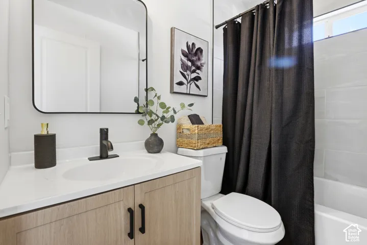 Bathroom featuring a vanity with light wood-finish cabinetry, a white countertop with an integrated basin, a matte black faucet, and a rectangular mirror with a rounded black frame, complemented by tile shower surrounds