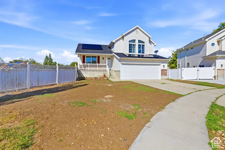 Multi-level exterior featuring light-toned horizontal siding, integrated roof-mounted solar panels, an elevated front porch with white railing, and an attached two-car garage