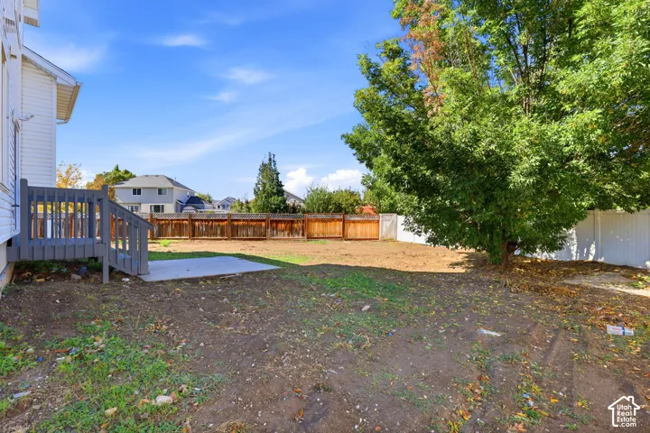 Rear yard featuring a raised deck, concrete patio, wood-slat privacy fencing, and mature trees