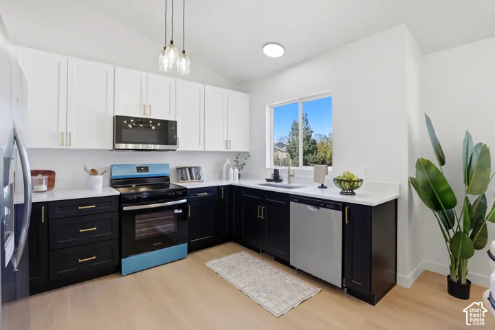 Kitchen featuring two-tone cabinetry, stone-finish countertops, stainless steel appliances, pendant lighting, and wood-finish flooring