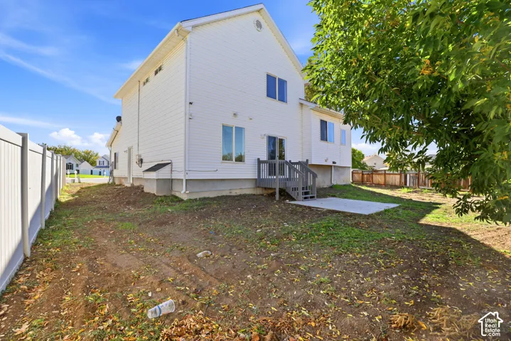 Two-story residence with white siding, rear concrete patio, wooden deck stairs, and vinyl privacy fencing