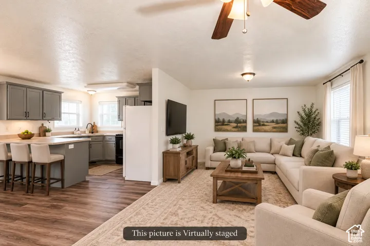Open-concept interior featuring gray kitchen cabinetry, a breakfast bar, wood-finish flooring, and a ceiling fan