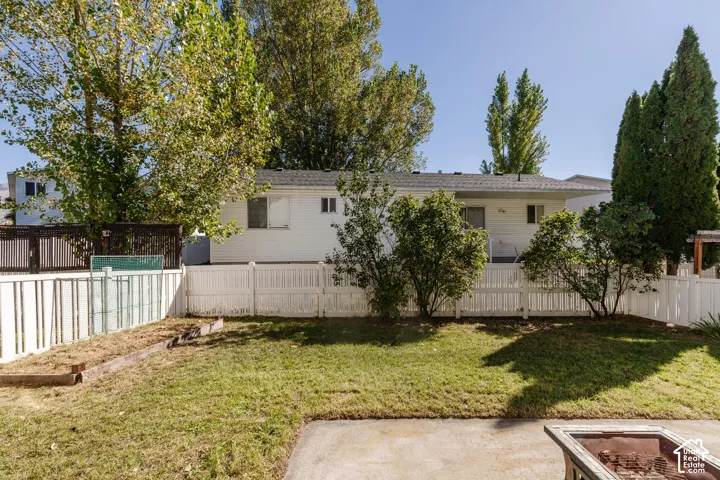Backyard featuring a concrete patio, white vinyl fencing, raised garden bed, and mature trees