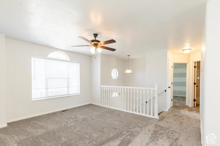 Carpeted flooring, ceiling fan with integrated light fixture, arched window, staircase with white railing, and decorative octagonal window