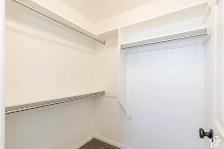 Walk-in closet featuring white built-in shelving, dual-level metal hanging rods, and neutral carpeting