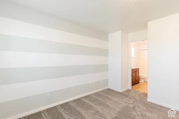 Room featuring horizontal-striped wall treatment, wall-to-wall carpet, and entry into a bathroom with a wood-finish vanity and tile flooring