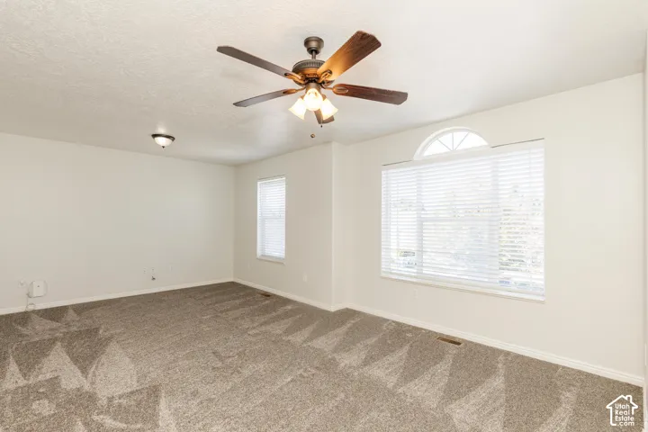 Interior space featuring neutral wall tones, carpeted flooring, a ceiling fan with integrated lighting, and a large window accented by an arched transom