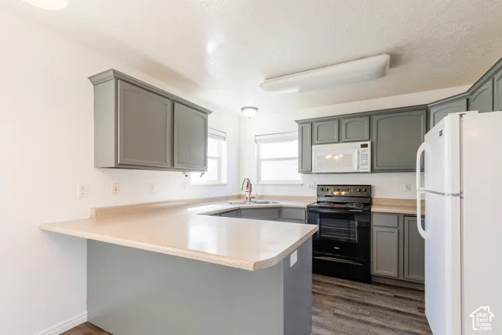 Kitchen featuring gray shaker-style cabinetry, solid-surface countertops, wood-finish flooring, and a peninsula layout