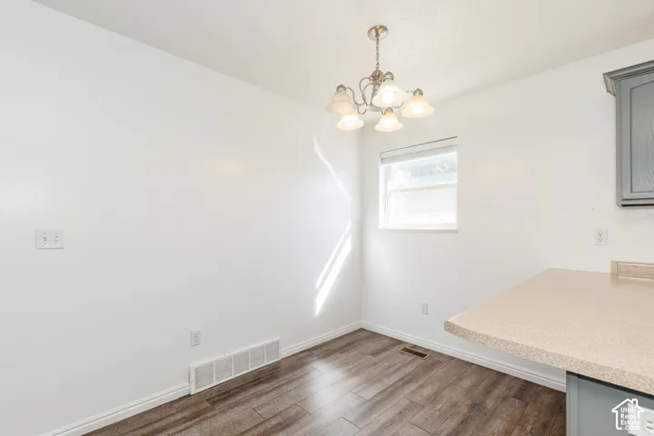 Wood-finish flooring, multi-light chandelier, neutral wall finish, and solid-surface countertop with grey built-in cabinetry